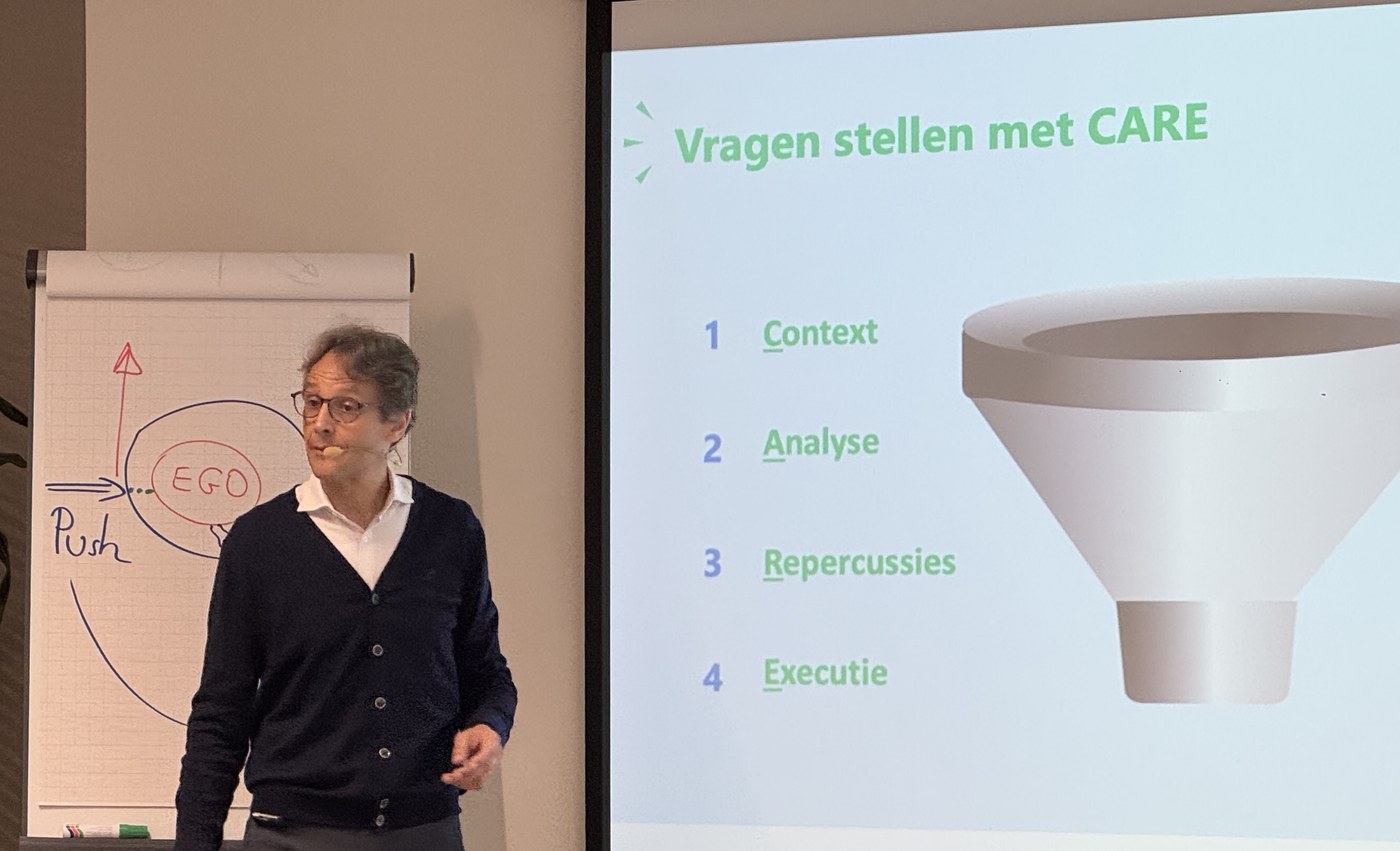 Vincent Flament van Valorize Solutions begeleidt een sessie in het Nederlands, met een flipchart en een slide over vragen stellen met CARE
